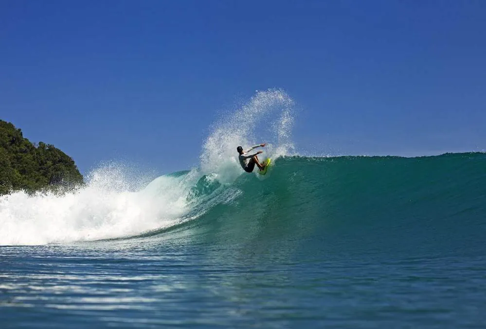 Surfer riding perfect turquoise wave at Occy's Left surf break in Sumba, Indonesia