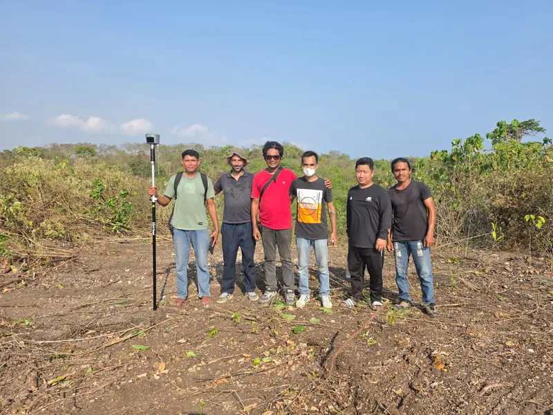 L’équipe pose sur le terrain défriché avec le géomètre et sa balise GNSS