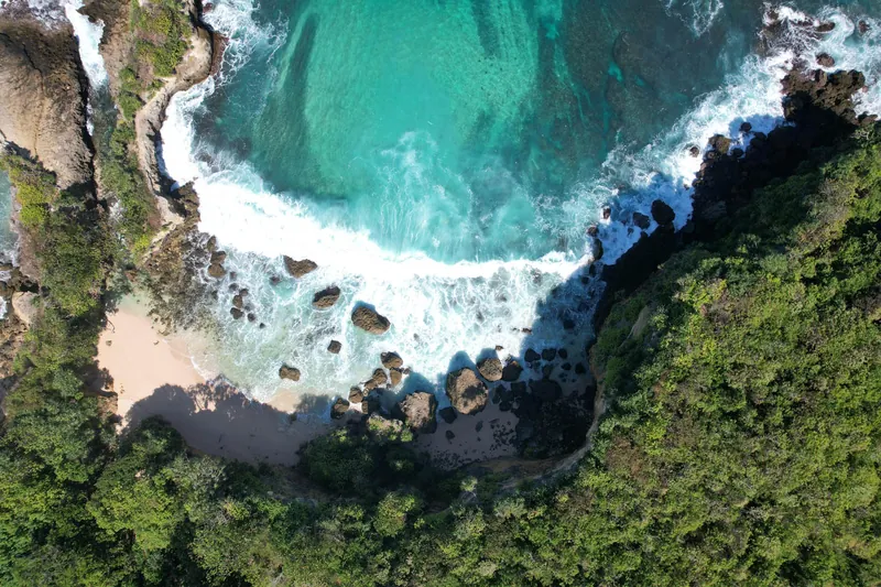 Aerial view of Kabisu's hidden beach and turquoise waters surrounded by lush cliffs in Southwest Sumba