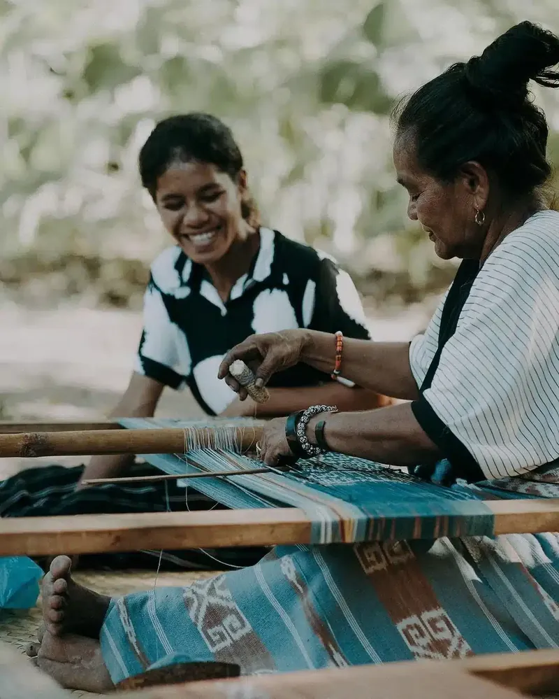 Two Sumbanese women weaving ikat cloth on a backstrap loom, symbolizing tradition and women’s empowerment.
