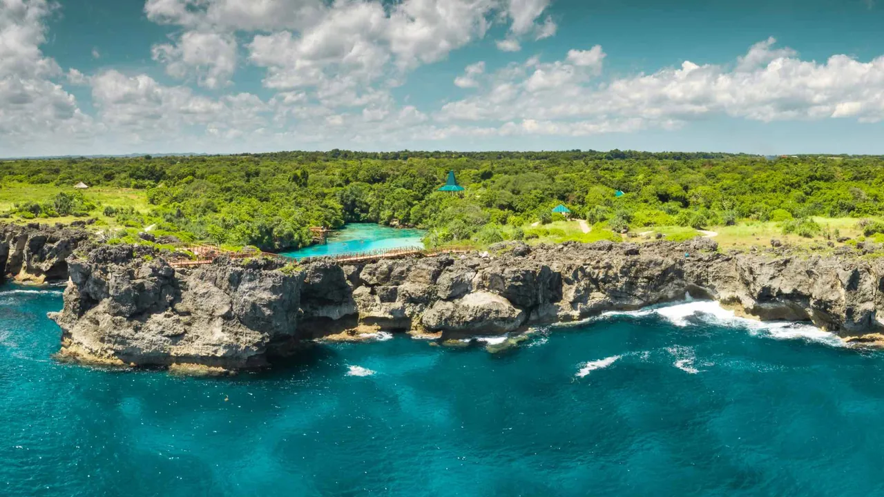 Aerial view of rugged cliffs and a bright turquoise lagoon surrounded by dense green forest on Sumba, Indonesia.