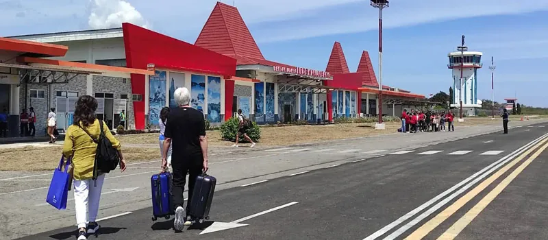 Passengers walking with luggage in front of Tambolaka Airport terminal on Sumba island.